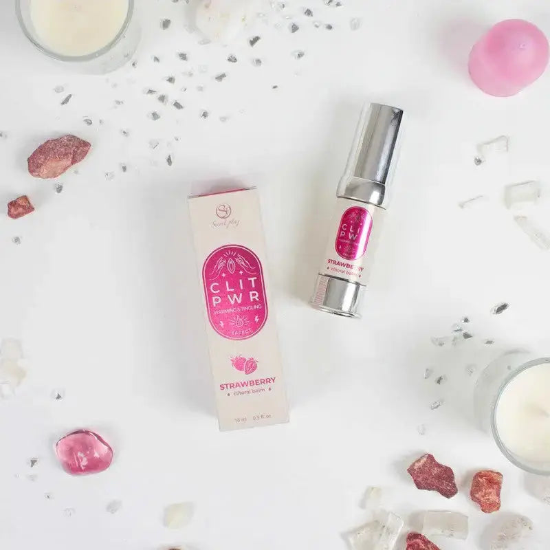 Baume clitoris Clit Pwr Fraise présenté avec son emballage sur une surface décorée de cristaux et de bougies.