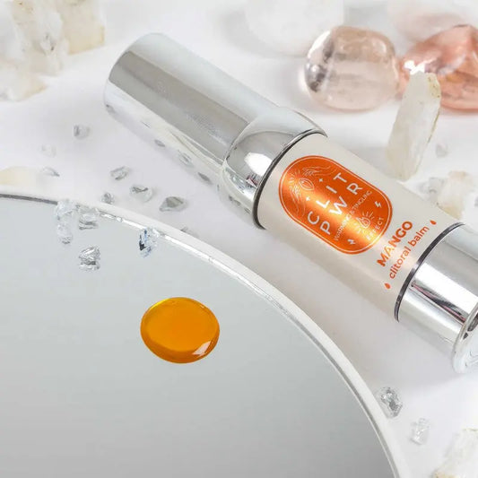 Baume clitoris Clit Pwr Mangue posé sur un miroir avec des cristaux et une goutte d'huile sur la surface.
