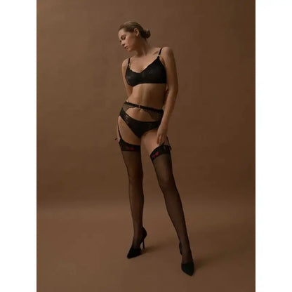 Femme portant des bas sexy Lola de Fiore avec des nœuds rouges, lingerie noire, sur fond marron.