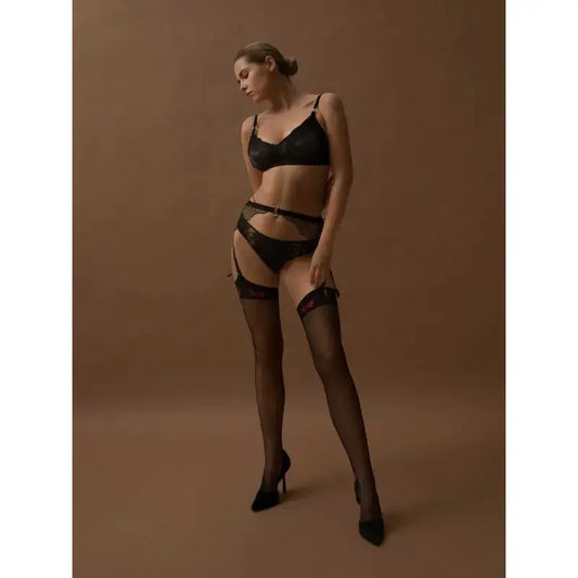 Femme portant des bas sexy Lola de Fiore avec des nœuds rouges, lingerie noire, sur fond marron.