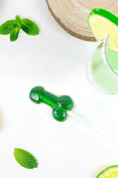 Sucette pénis goût mojito alcoolisée sur une table avec des feuilles de menthe et des quartiers de citron.