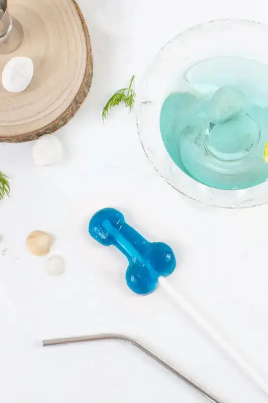 Sucette pénis alcoolisée goût gin tonic avec un cocktail bleu, accessoire amusant pour soirées.