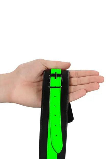 Menottes phosphorescentes Ouch! montrées avec une main, couleur noire et verte, pour des jeux coquins lumineux.